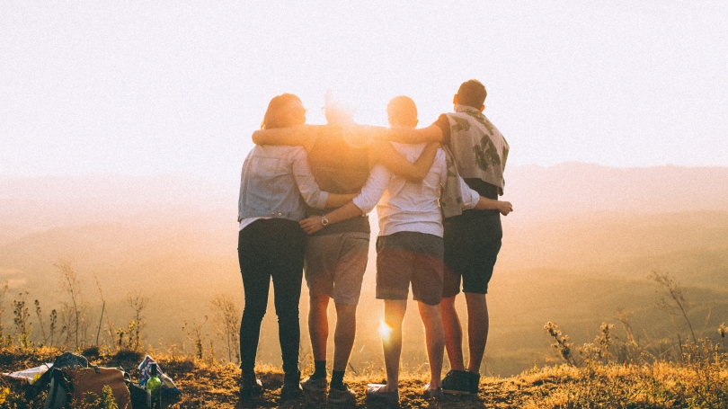 backlit image of four people standing together with their backs to the camera